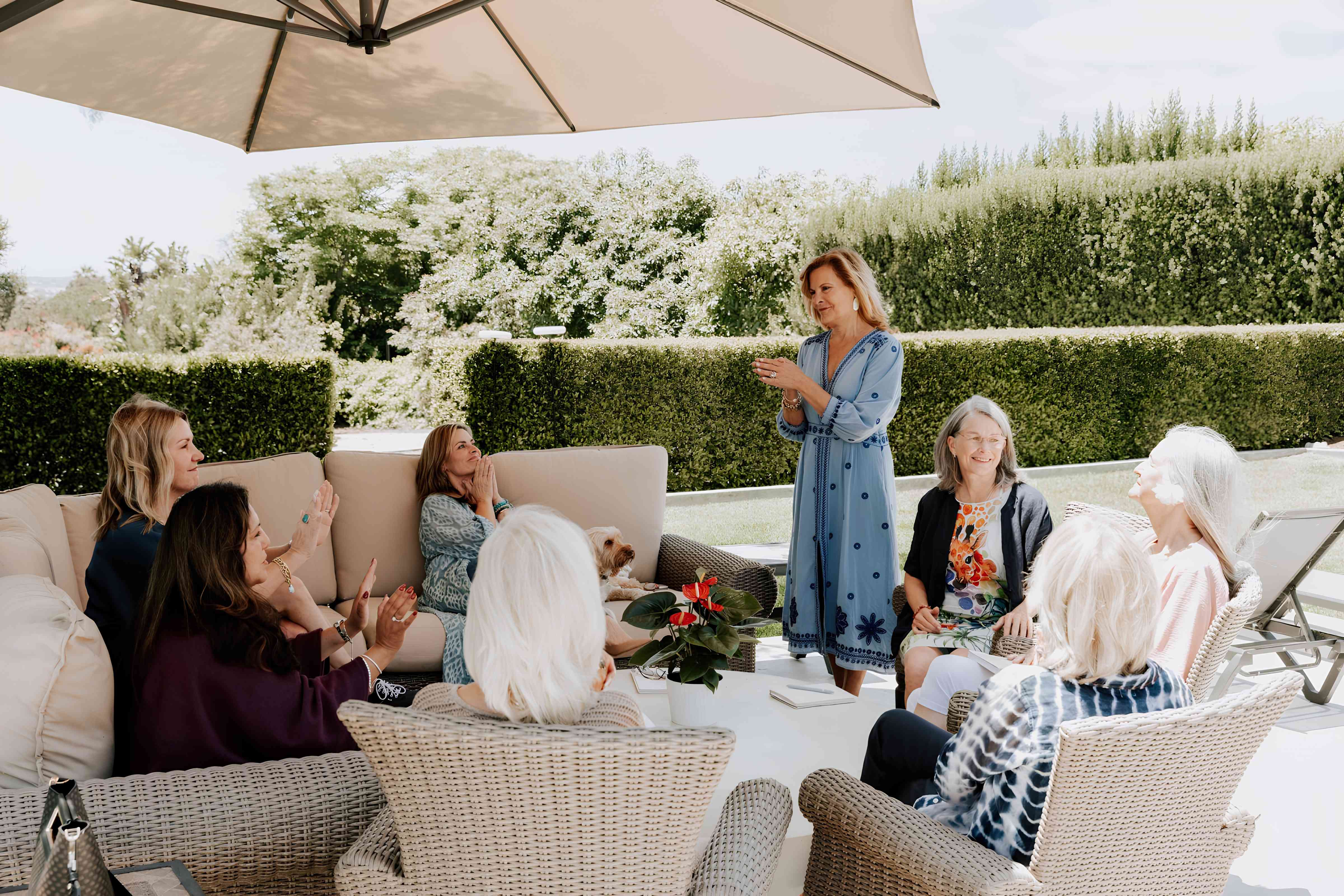 Leighanne standing and speaking with a group of women seated on patio furniture at a garden retreat
