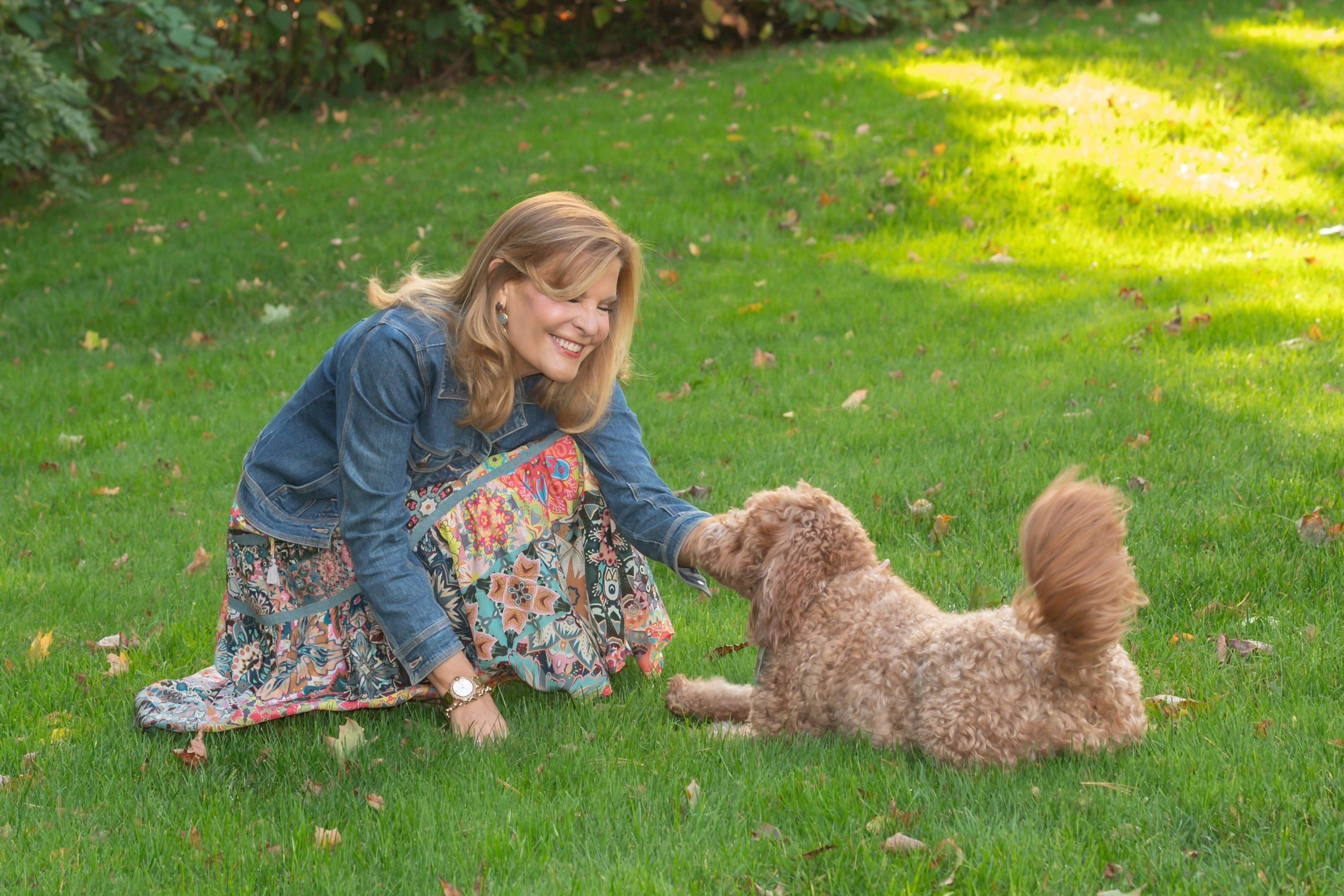 Leighanne kneeling on a sunlit autumn lawn playing with her curly apricot doodle dog