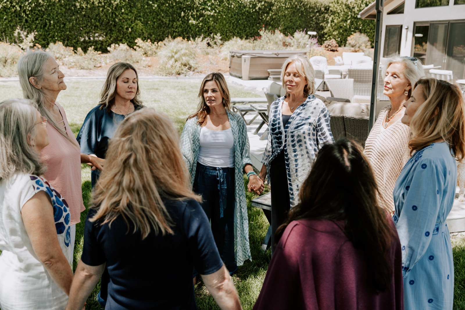 A circle of women holding hands on a garden lawn in a reflective moment at a retreat