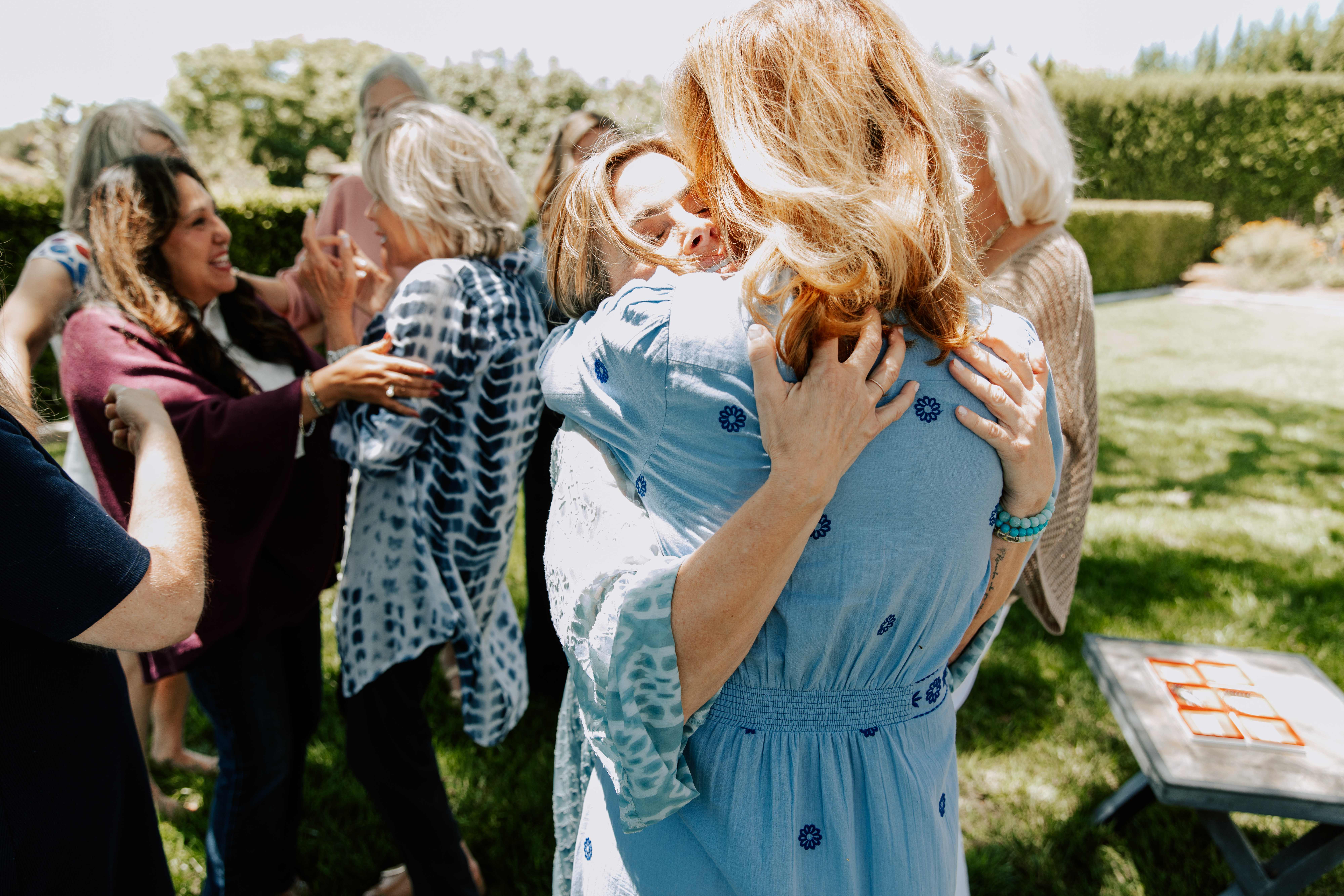 Two women embracing closely while other women greet each other behind them