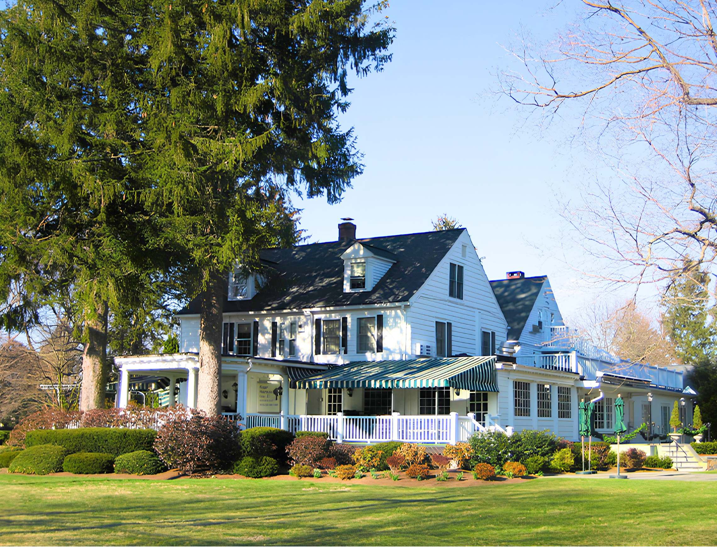 The Roger Sherman Inn, a white New England colonial building with green-striped awnings, set behind manicured gardens and tall evergreens